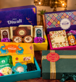 Four festive corporate Diwali gift hampers featuring colorful gift boxes, traditional sweets, dry fruit bites, snacks, and elegant green packaging, arranged closely together with glowing diyas and marigold flowers.