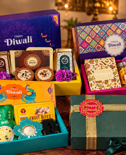 Four festive corporate Diwali gift hampers featuring colorful gift boxes, traditional sweets, dry fruit bites, snacks, and elegant green packaging, arranged closely together with glowing diyas and marigold flowers.
