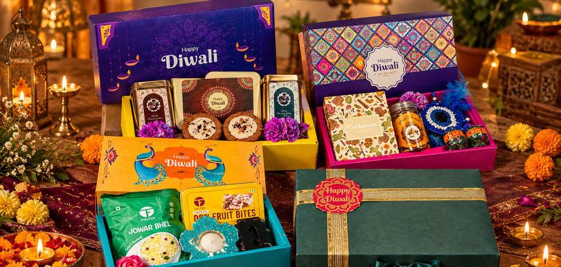 Four festive corporate Diwali gift hampers featuring colorful gift boxes, traditional sweets, dry fruit bites, snacks, and elegant green packaging, arranged closely together with glowing diyas and marigold flowers.